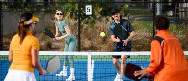 Four people engage in a lively doubles pickleball match, two on each side of the net, fully immersed and focused on the game at a well-maintained pickleball facility's outdoor courts.