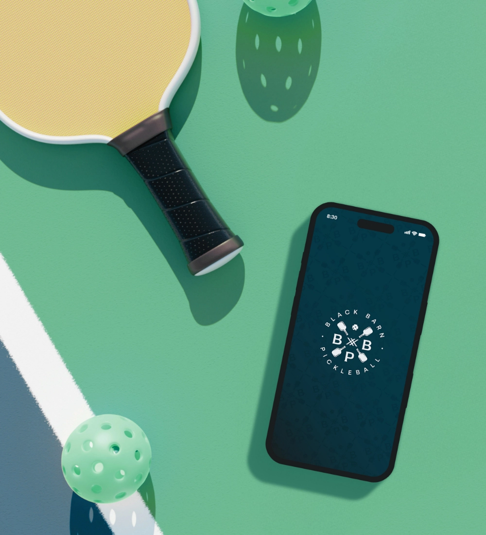 Black Barn Pickleball mobile app shown on a phone on a pickleball court.